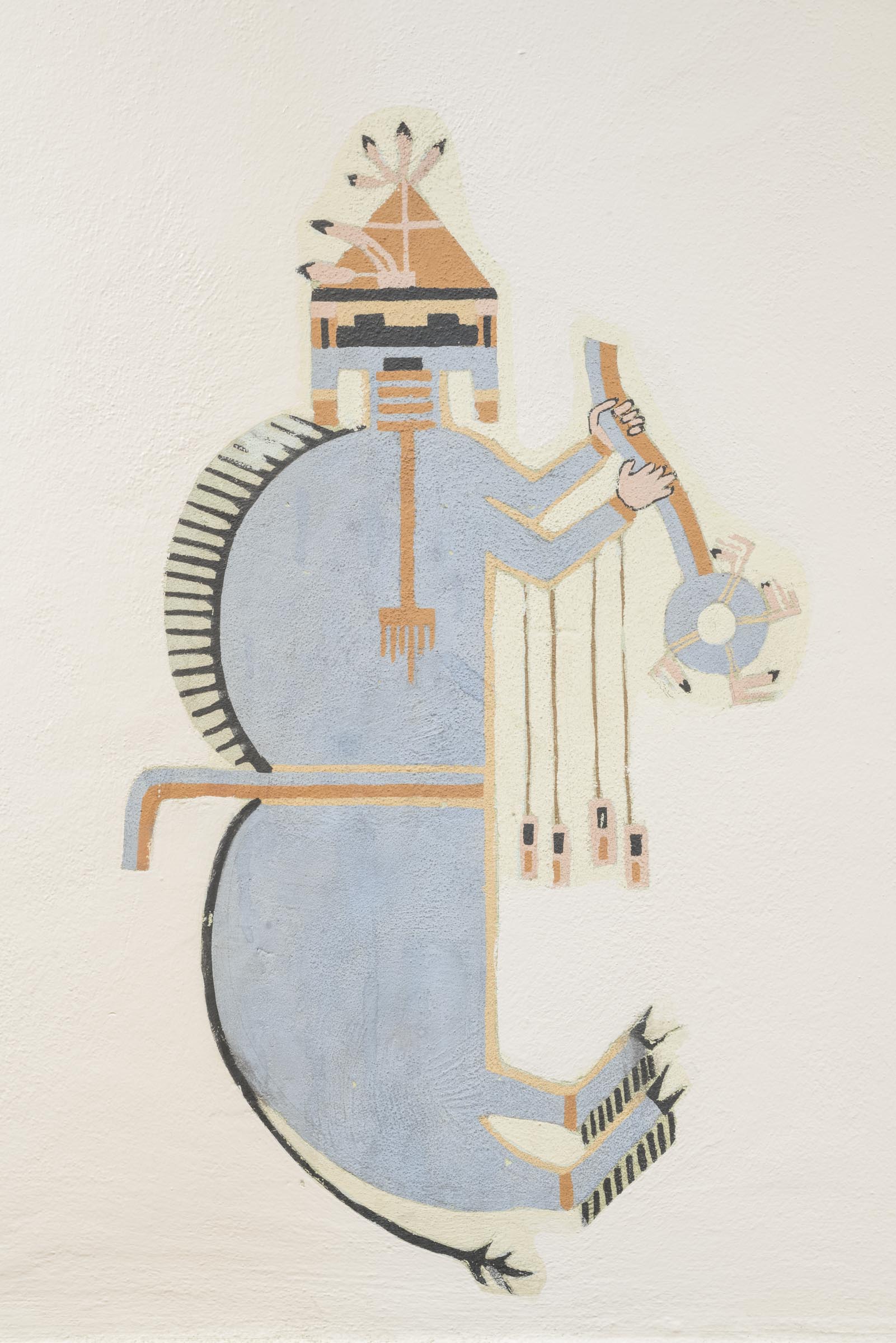 A photograph of a painting of a stylized, blue-colored figure on a light background. The figure is oriented vertically. It has a rectangular head with small black rectangles for the eyes and mouth and wears a light brown triangular hat adorned with feathers. It has two humps on its back, a pointy black mane, a thin black tail, and hoofed feet. Its arms are bent in front of its body and two peach-colored human hands hold a staff with a circular piece at its bottom.